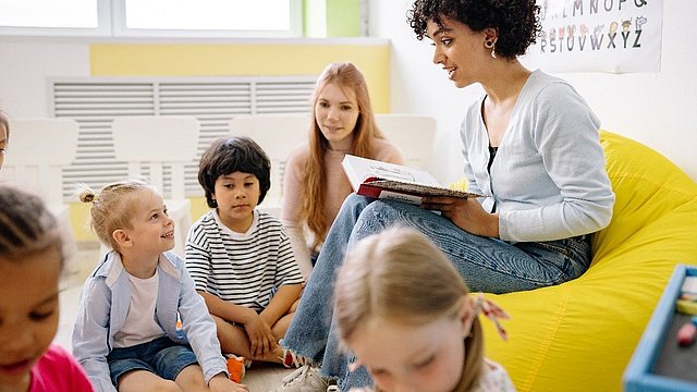 © Yan Krukov Lehrerin liest Kindergartenkindern etwas vor.