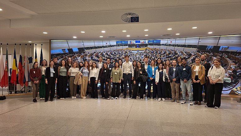 Das Bild zeigt eine Gruppe von Jungen und Mädchen, die vor dem Plenarsaal des Europäischen Parlaments in Brüssel und den Flaggen für ein Foto posieren. 