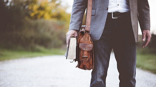 Professore con borsa a tracolla e un libro in mano.