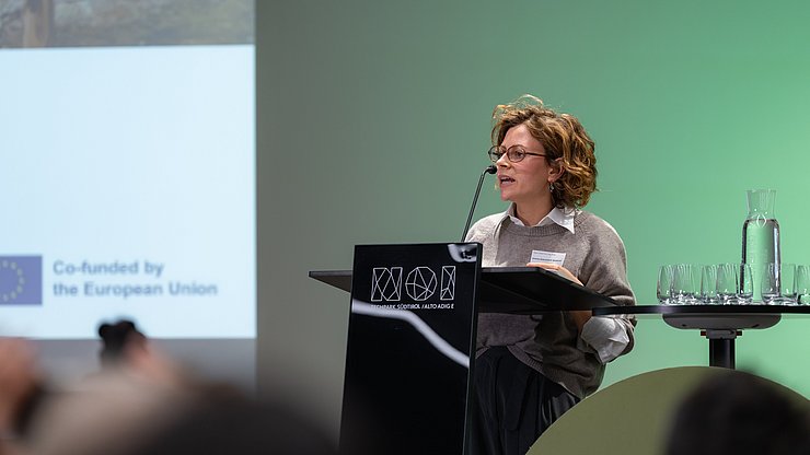 Person spricht am Pult vor einer Präsentation