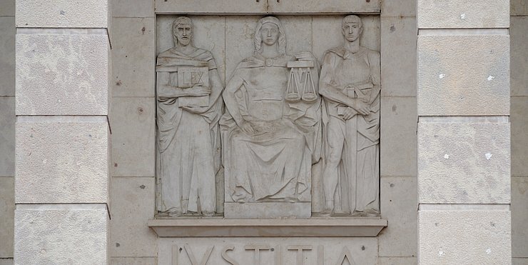 Die sitzende Iustitia (Gerechtigkeit) am Gebäude des Bozner Landesgerichts, das ab 1939 errichtet wurde. Dieser fehlt auffälligerweise die Augenbinde, das Attribut, das für die Unparteilichkeit der Justiz steht.