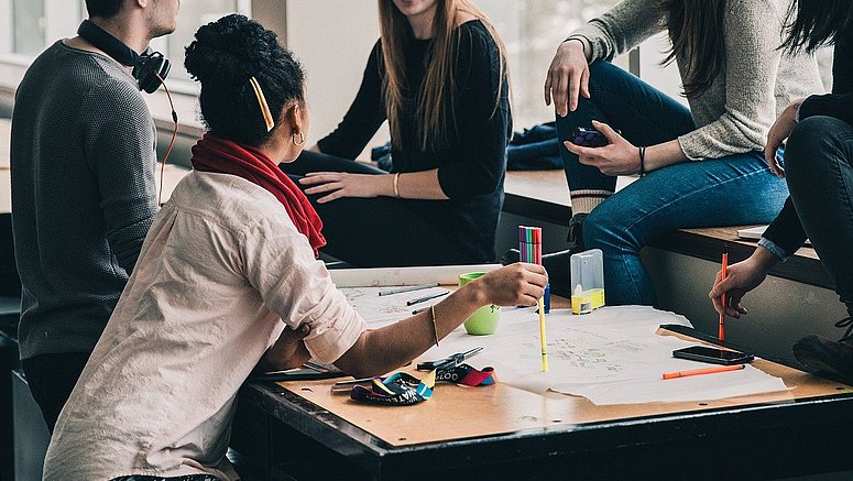 In einem Klassenzimmer arbeiten fünf Schüler konzentriert an einem Gruppenprojekt. Sie tauschen Ideen aus, diskutieren lebhaft und halten ihre Gedanken aufmerksam fest. 