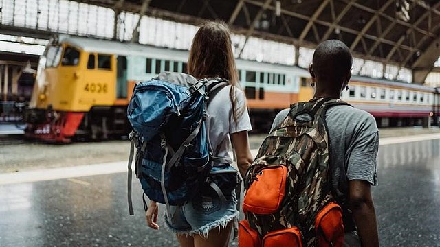 © Pexels/KetutSubiyanto Zwei junge Leute mit Rucksäcken auf dem Rücken sind bereit, um zu einer Zugreise aufzubrechen.