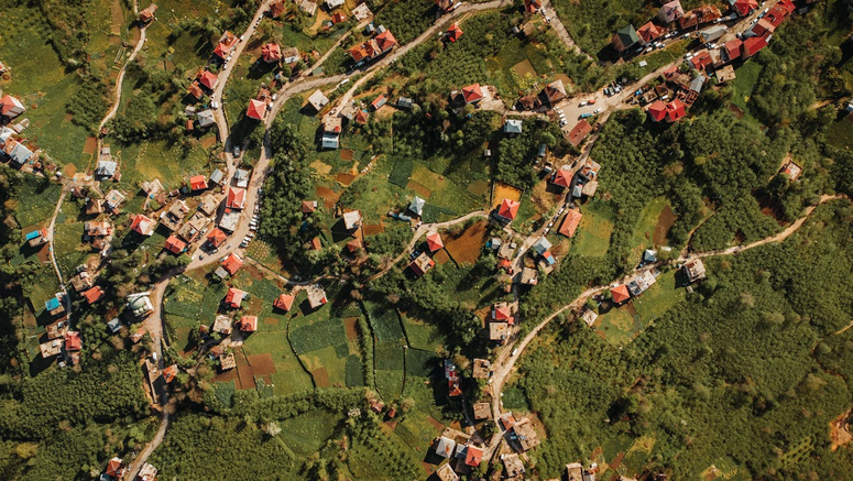 Drohnenaufnahme eines Dorfes auf dem Land mit farbenfrohen Feldern und Häusern, die eine friedliche Landschaft zeigen.