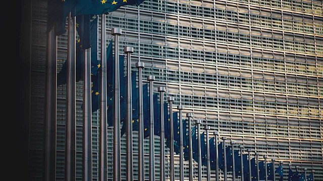 © Unsplash/ChristianLue Fahnen wehen vor dem Berlaymont-Gebäude, dem Sitz der Europäischen Kommission.