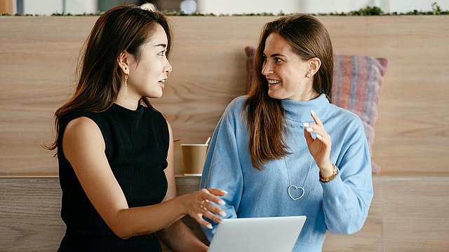 Zwei junge Frauen sitzen miteinander vor einem Laptop und unterhalten sich.