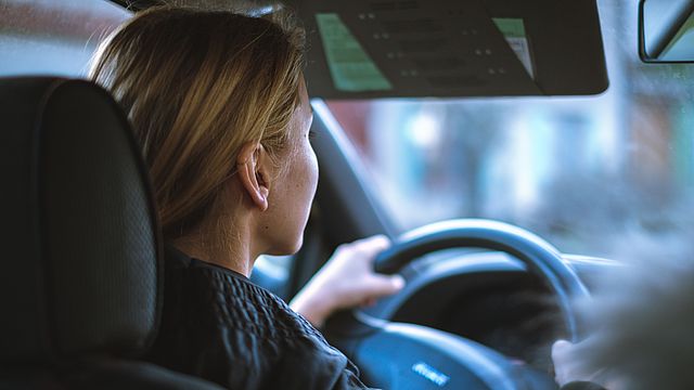 Eine junge Fahrerin steuert konzentriert, mit beiden Hände am Lenkrad, ihr Auto.