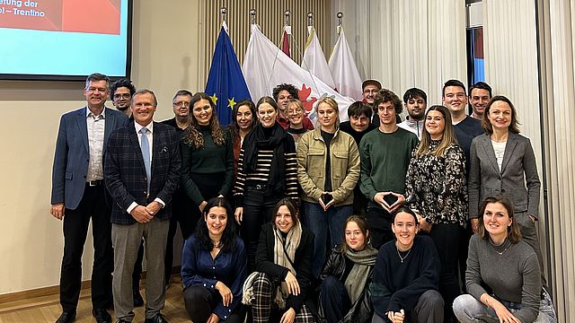 Das Bild zeigt die Teilnehmer*innen der Tiroler Journalismusakademie zusammen mit dem Büroleiter Dr. Richard Seeber. Im Hintergrund sind die Flaggen von Tirol, Südtirol, Trentino, der Europäischen Union und der Europaregion zu sehen.