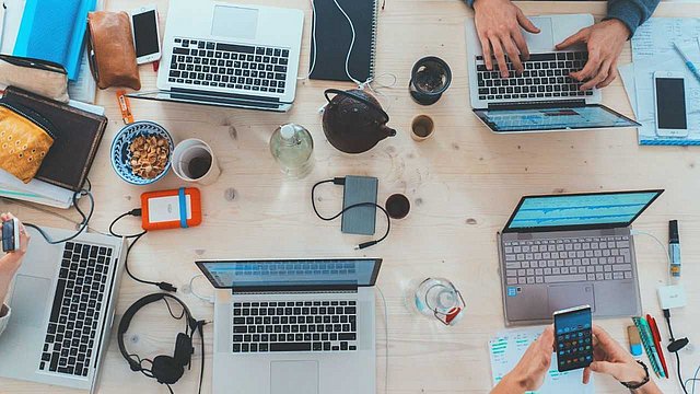 © Unsplah/Marvin_Meyer Menschen arbeiten an einem Tisch mit digitalen Geräten.