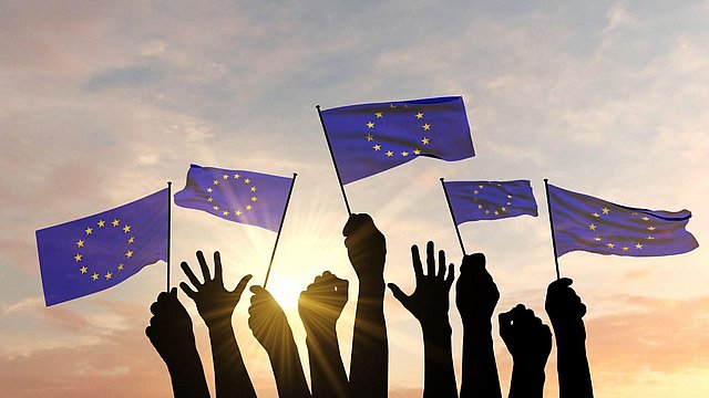 © ECIT Foundation Auf dem Bild sind Hände und Arme von Menschen zu sehen, die Flaggen der Europäischen Union halten.