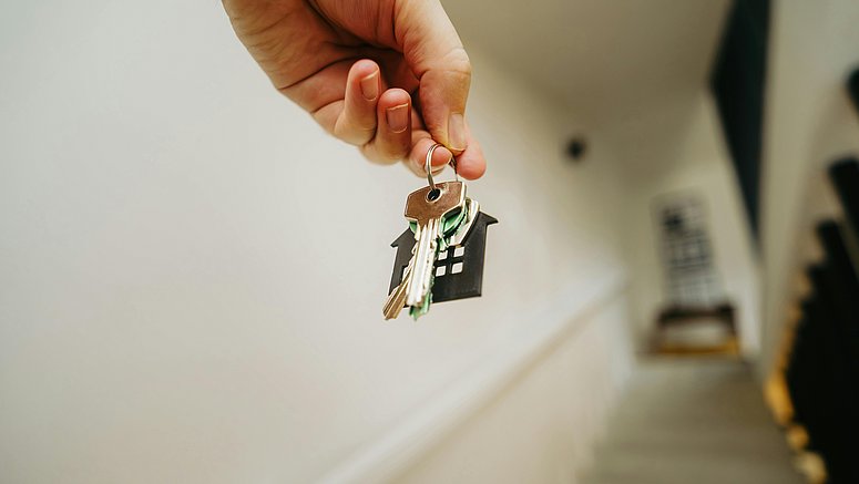 Eine Person hält einen Schlüsselbund mit einem kleinen Hausanhänger in der Hand. Das Bild steht für den Wunsch nach einem eigenen Zuhause und die wachsenden Herausforderungen auf dem Wohnungsmarkt.