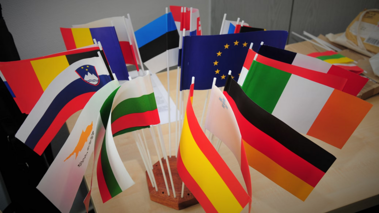 Flaggen der EU-Mitgliedstaaten dicht nebeneinander auf einem Tisch