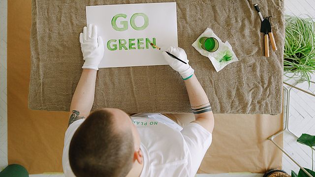 L'immagine mostra una persona dall'alto che sorregge un cartello con la scritta "GO GREEN!" in lettere verdi.