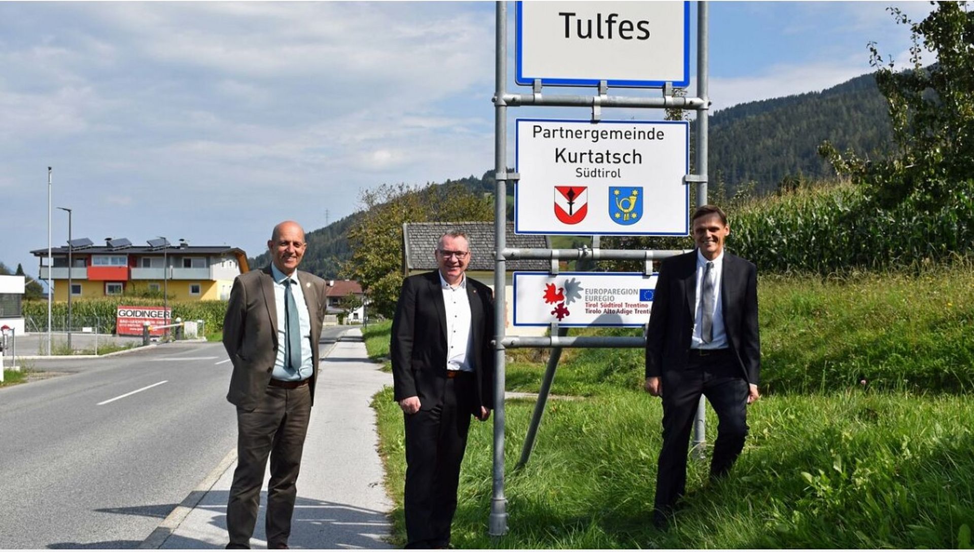 Il consigliere dell'Euregio Fritz Tiefenthaler, l'assessore tirolese con delega ai comuni LR Johannes Tratter e il sindaco di Tufles, Martin Wegscheider, davanti al cartello Euregio del partenariato tra comuni.