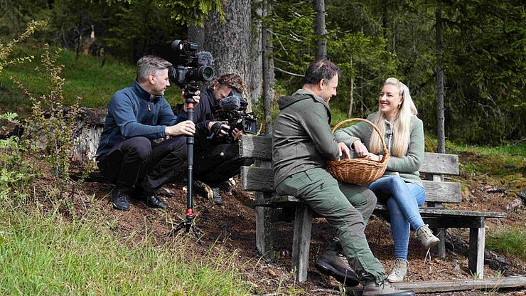 Utilizza il bosco come scrigno di sapori alpini: Andrea Irsara (a sinistra sulla panchina) con la presentatrice Karin Gschnitzer durante le riprese di "Euregio in tavola".