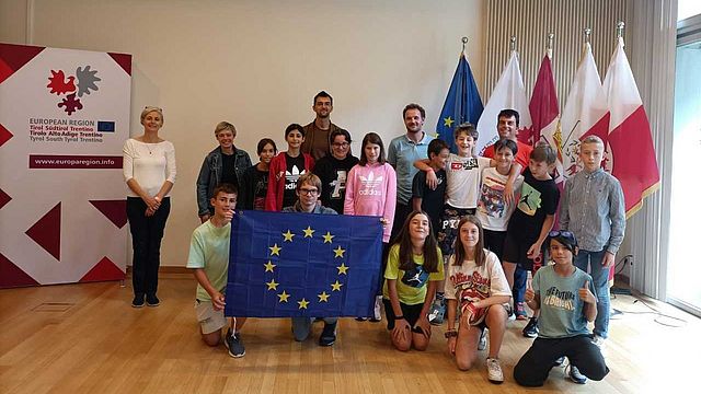 Schülerinnen und Schüler, Lehrerinnen und Lehrer und Euregio-Mitarbeiter bei einem Gruppenfoto vor den regionalen und europäischen Flaggen in der Vertretung in Brüssel.