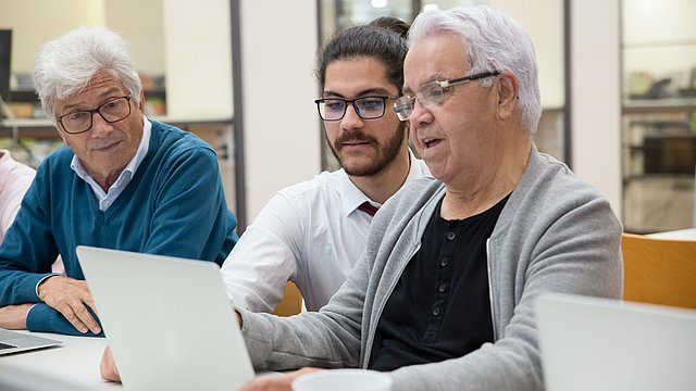 Descrizione non vedenti: un giovane spiega a un anziano davanti a un computer 