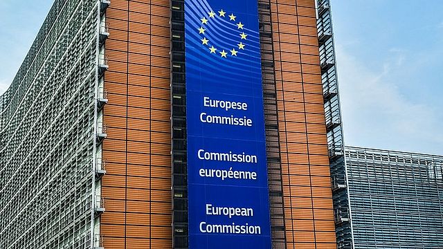 Gebäude der Europäischen Kommission mit einem Banner mit dem Namen der Kommission in mehreren Sprachen an der Fassade.