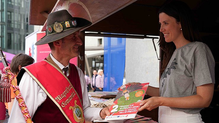 Ein Musikant informiert sich am Euregio-Stand bei Mitarbeiterin Costanza Pozzo. 
