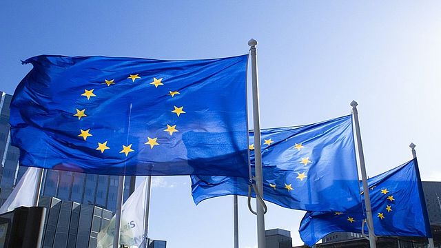 L'immagine mostra tre bandiere dell'Unione Europea che sventolano 