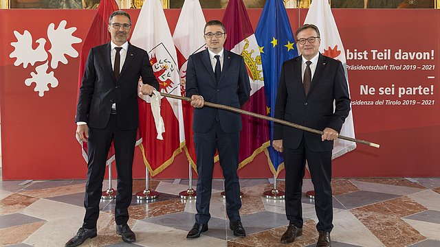 © Land Tirol/Die Fotografen il Presidente Platter consegna il bastone itinerante simbolico al Presidente dell'Euregio Fugatti.