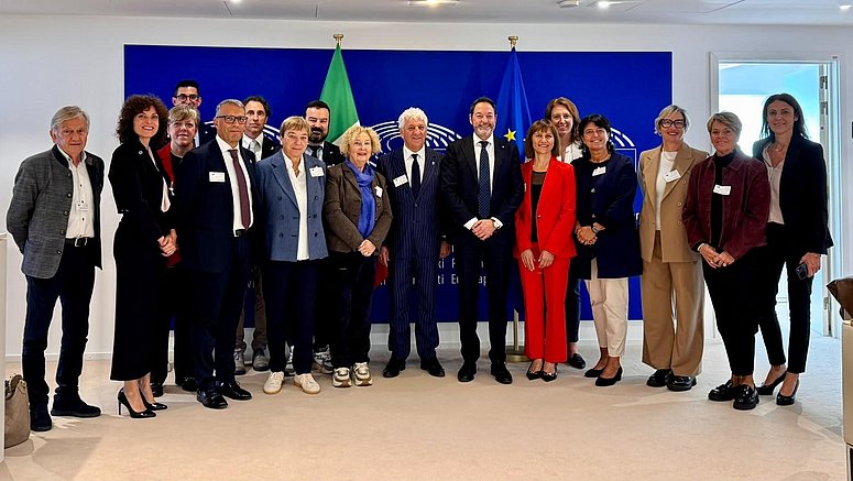 Mitglieder des Landtags der Autonomen Provinz Trient und der Generalsekretär des Europäischen Parlaments, Alessandro Chiocchetti, posieren für ein Foto vor den Fahnen der Europäischen Union und Italiens.