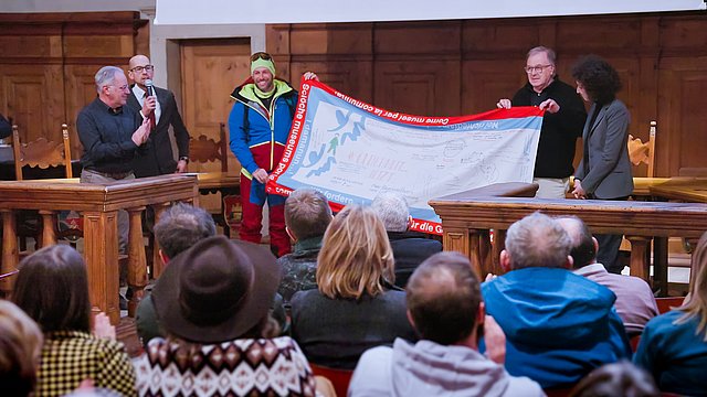 Inaugurazione della mostra "Il bosco e le piante nella crisi climatica attuale: il caso della Magnifica Comunità di Fiemme", da sx:  Elio Vanzo (collaboratore della Magnifica Comunità di Fiemme), Tommaso Dossi (Responsabile archivio della Magnifica Comunità di Fiemme), Danilo Callegari (alpinista e avventuriero estremo) il quale regge la bandiera assieme allo scario della Magnifica Comunità Mauro Gilmozzi ed Elisa Bertò (Segretariato Generale Euregio).