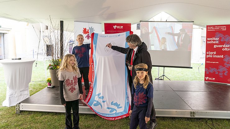 Eröffnung des Euregio-Museumsjahrs am 29. März 2025: Der Direktor der Hofburg Brixen Peter Schwienbacher hinterlässt die ersten Spuren auf der Museumsjahr-Wanderfahne.
