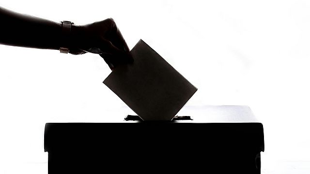 Eine Hand gibt einen Wahlzettel in die Wahlurne, die die EU-Wahlen repräsentieren sollen.