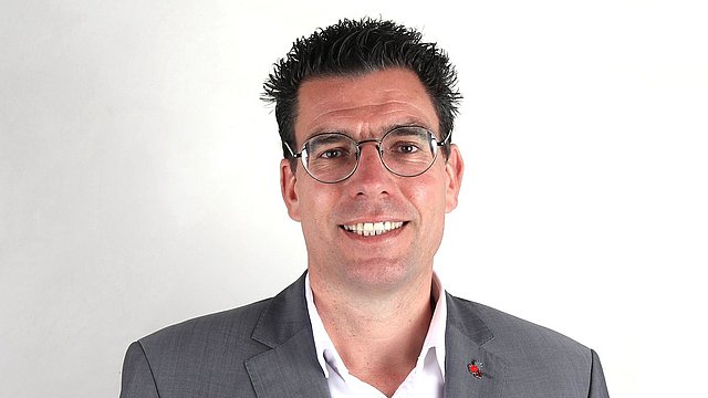 Foto von Matthias Fink mit Brille, weißem Hemd und grauem Anzug mit weißem Hintergrund