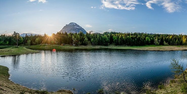 Un lago di montagna circondato da una foresta e nel sottofondo una montagna al tramonto del sole. 