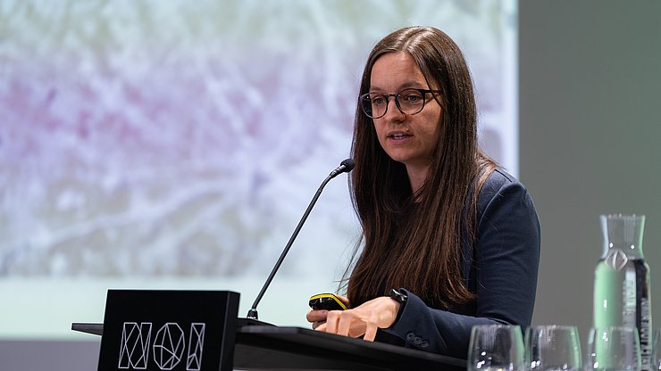 Person spricht am Pult vor einer Präsentation