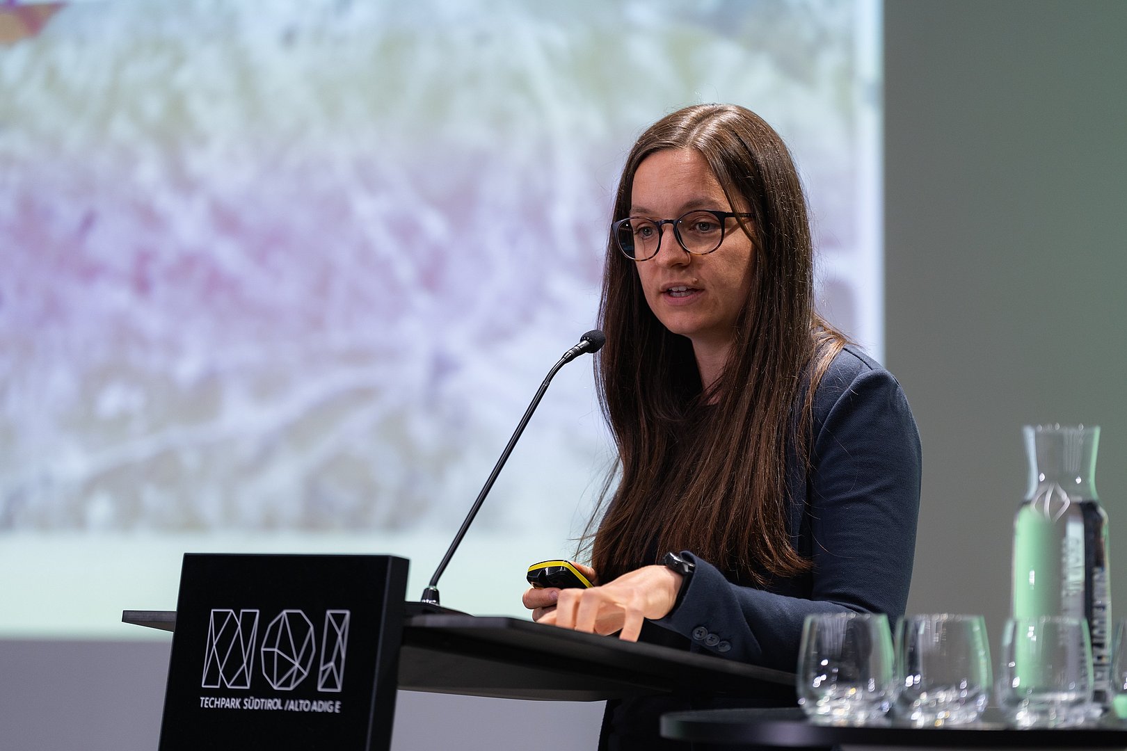 Person spricht am Pult vor einer Präsentation