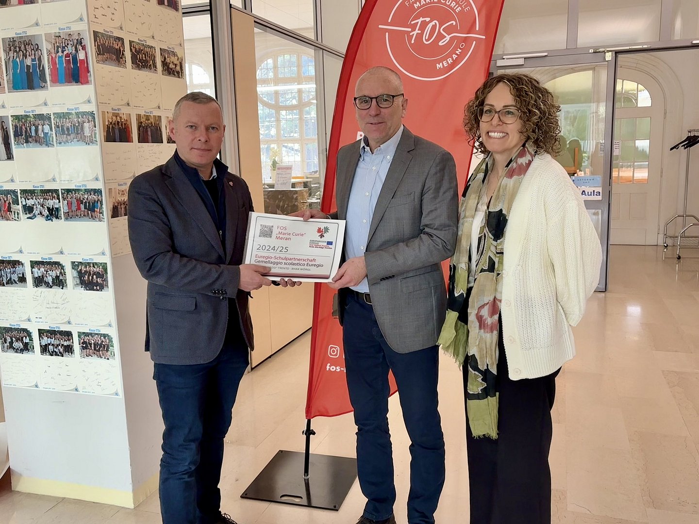 Il Segretario Generale dell'Euregio Christoph von Ach (sx) consegna a Merano la targhetta di riconoscimento “Gemellaggio scolastico Euregio” al Direttore dell'Istituto FOS Markus Dapunt e all'insegnante Barbara Pircher