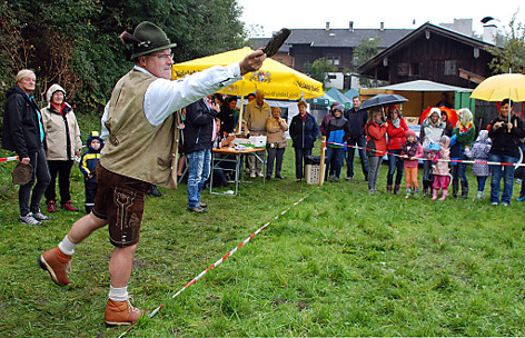Ein Mann in Lederhose wirft eine Kuhflade wie ein Diskus unter den Blicken der Zuseher. 